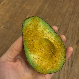 A green avocado half, sprinkled with an adobo spice blend, in a person's hand.