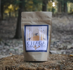 A brown paper package of chaga mushroom ground with a white, black, and earth-tone label, in front of a forest background